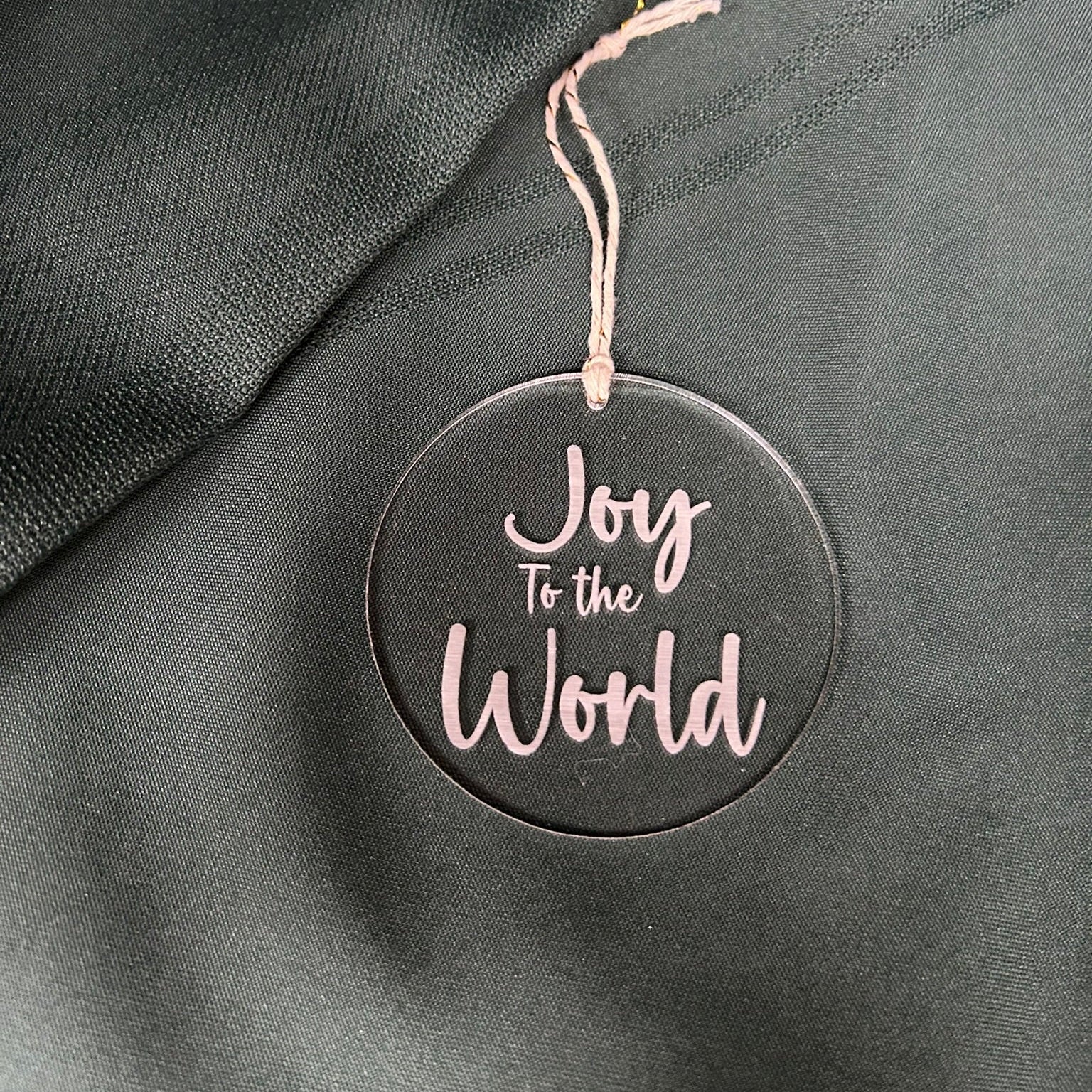 Round ornament with 'Joy To The World' text on a dark fabric background