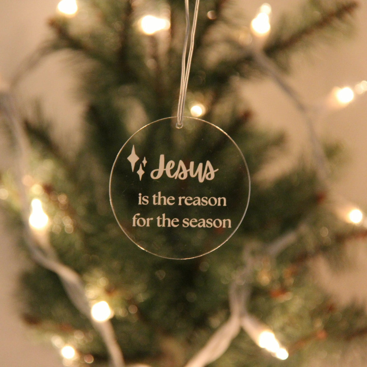 Decorative Christmas ornament with 'Jesus is the reason for the season' text on a blurred Christmas tree background.