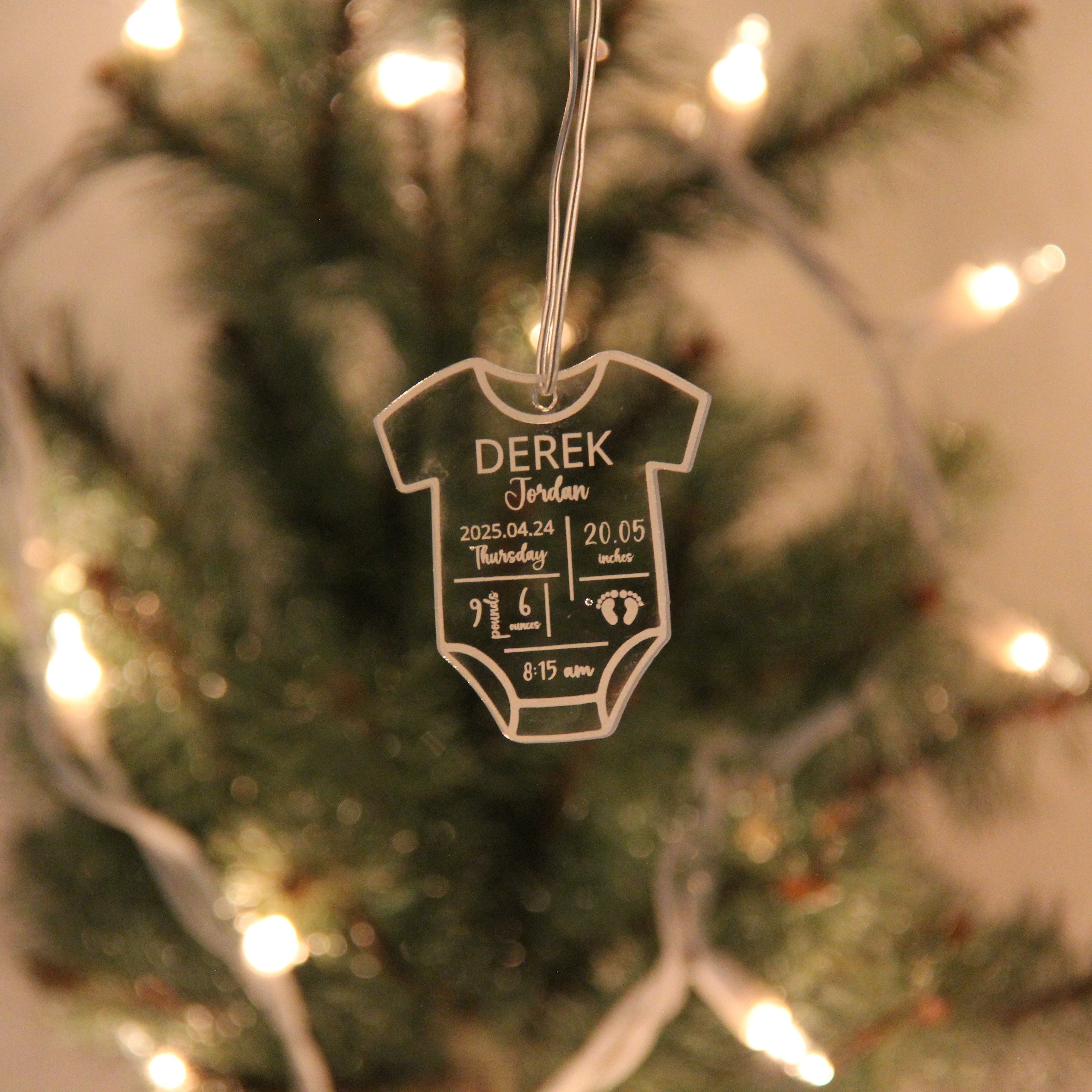 Decorative baby onesie ornament with personalized details on a Christmas tree.