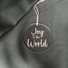 Round ornament with 'Joy To The World' text on a dark fabric background