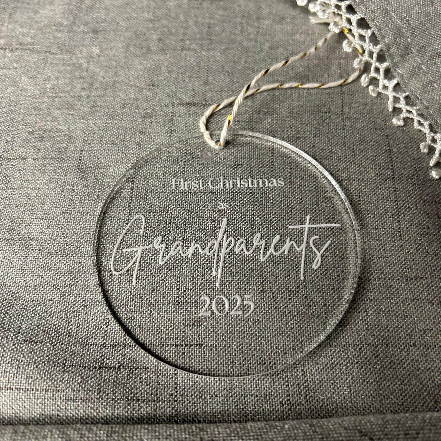 Round ornament with 'First Christmas as Grandparents 2023' text on a gray fabric background