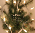 Decorative Christmas ornament with 'Jesus is the reason for the season' text on a blurred Christmas tree background.