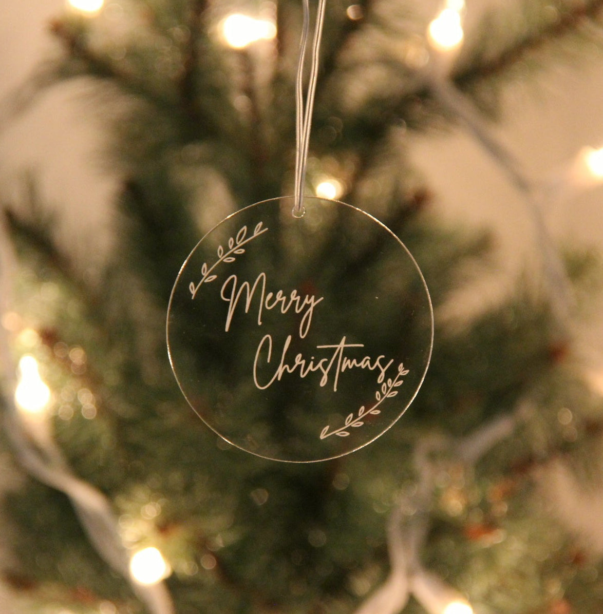 Clear Christmas ornament with 'Merry Christmas' text hanging on a decorated tree.