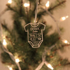 Decorative baby onesie ornament with personalized details on a Christmas tree.